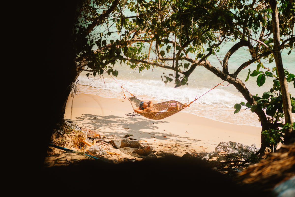 A guest resting in a woven hammock at the water's edge on a Keelooma beach camp, Palawan