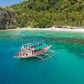 Keelooma's premium outrigger boat anchored off a palm-lined white sand beach on an El Nido island hopping tour, Palawan