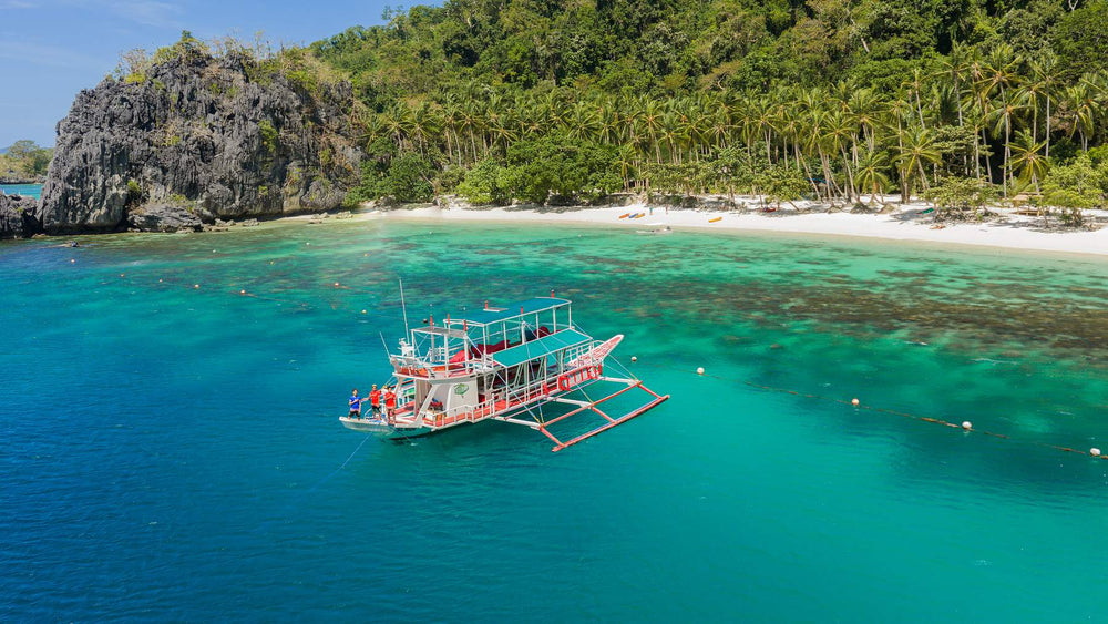 Keelooma's premium outrigger boat anchored off a palm-lined white sand beach on an El Nido island hopping tour, Palawan