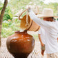 A Keelooma guide pouring well water from a wooden bucket into a banga, the clay jar that keeps water cool, at Kaseledan Farm, El Nido, Palawan