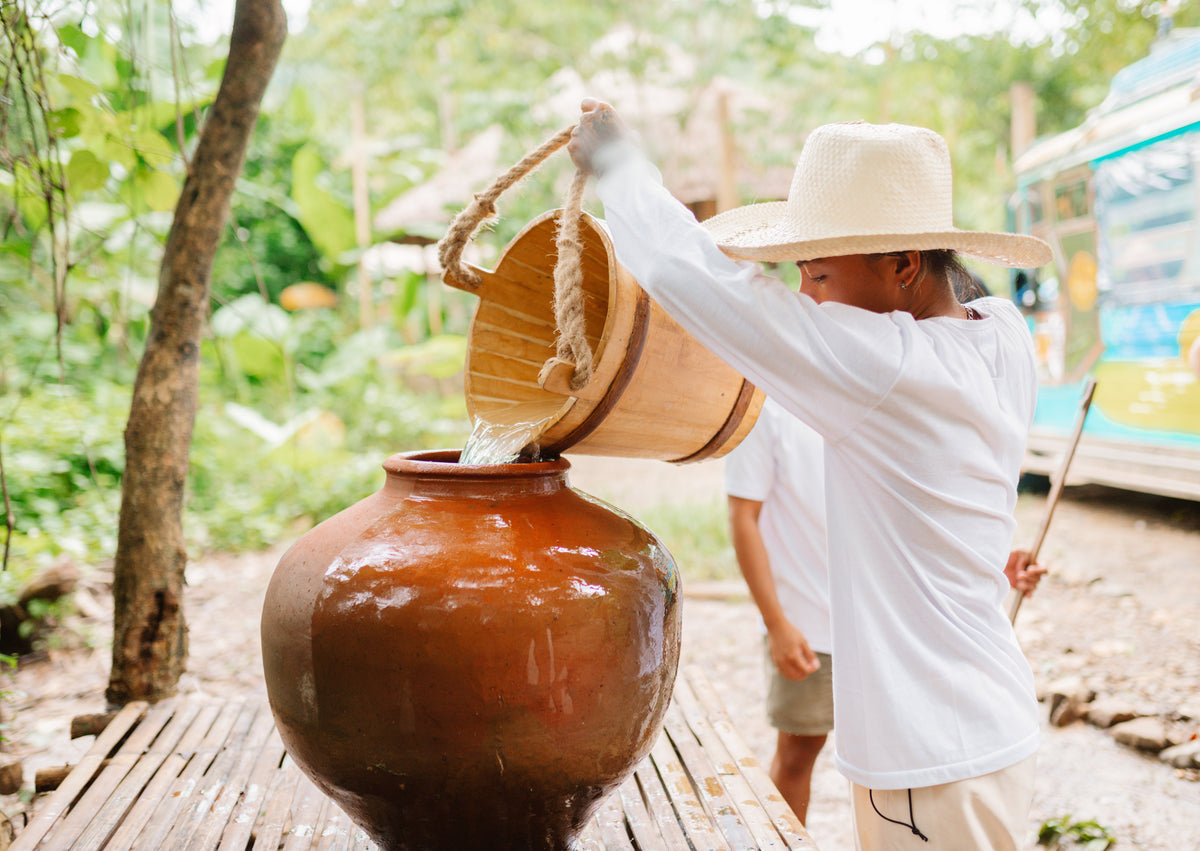 A Keelooma guide pouring well water from a wooden bucket into a banga, the clay jar that keeps water cool, at Kaseledan Farm, El Nido, Palawan