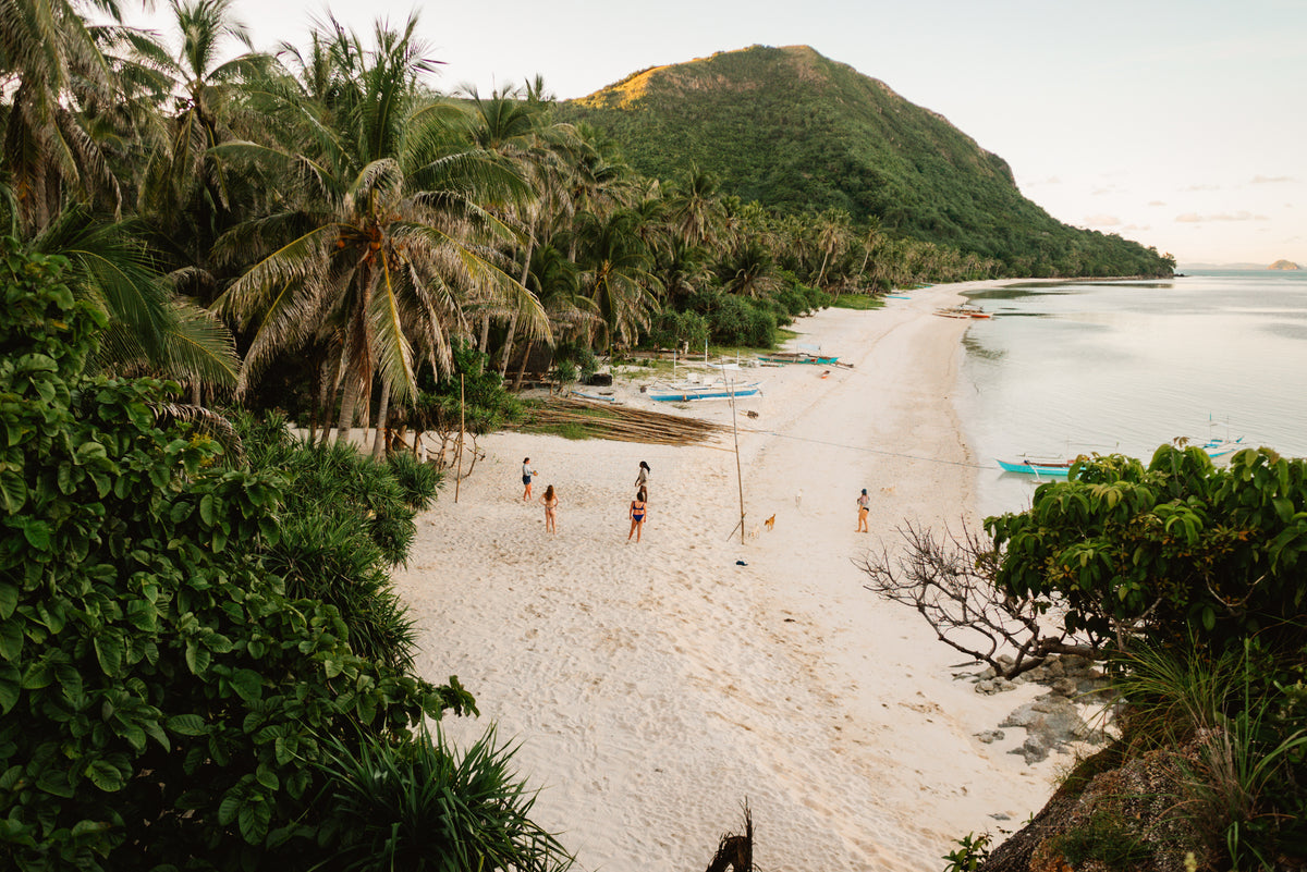 A palm-fringed beach with outrigger boats and a Keelooma camp along the shoreline, seen from above, Palawan