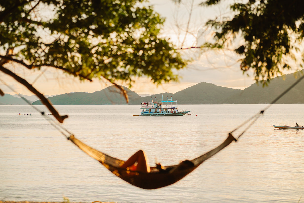 The Keelooma expedition boat anchored offshore at sunset, seen from a hammock on the beach, Palawan