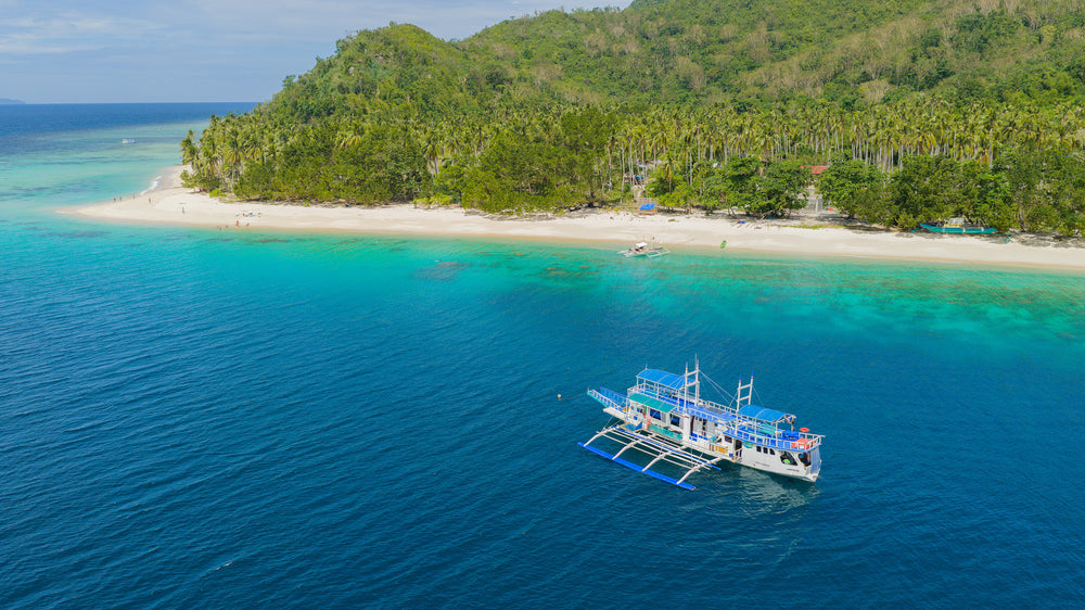 The Keelooma expedition boat, an outrigger banka, moored off Iloc Island in Linapacan, with a white-sand beach and coral reef on the El Nido to Coron route, Palawan