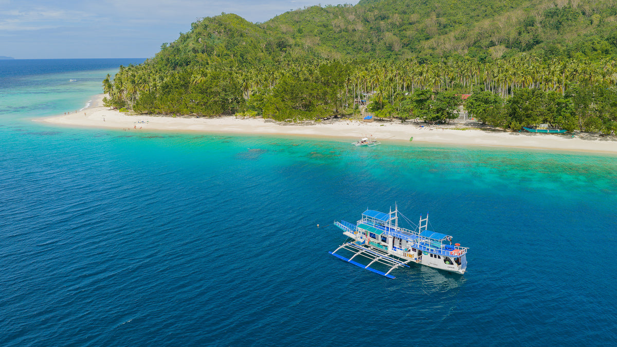 The Keelooma expedition boat, an outrigger banka, moored off Iloc Island in Linapacan, with a white-sand beach and coral reef on the El Nido to Coron route, Palawan