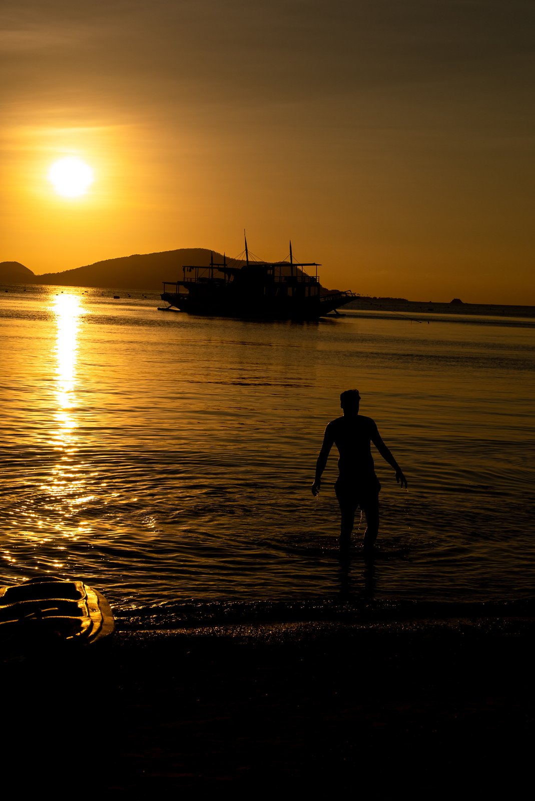 A guest wading ashore at sunset with the Keelooma expedition boat, Palawan