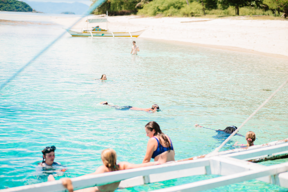 Guests snorkelling in shallow turquoise water beside the expedition boat, Coron to El Nido route, Palawan