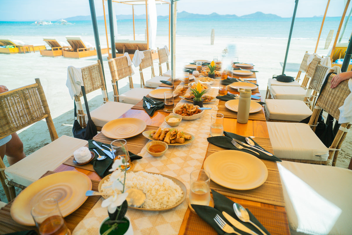 A beachfront lunch table set for the Keelooma jeepney tour at Ursula Beach Club, with rice, lumpia and shared dishes facing the sea, Sibaltan, El Nido, Palawan